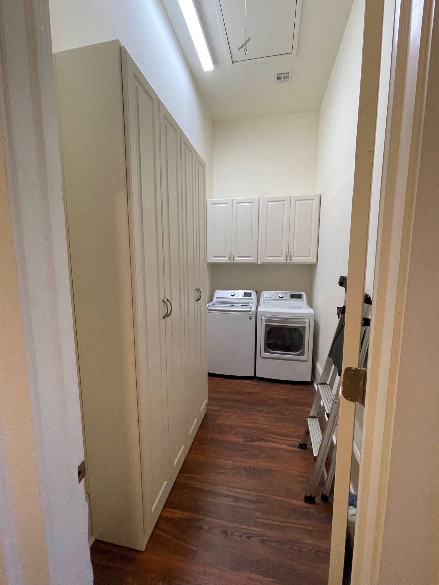Laundry room with washer, dryer, cabinets, and tall storage on left. Dark wood-look floor.