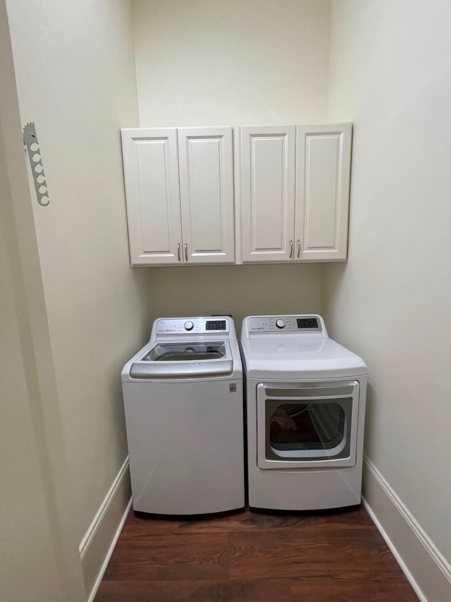 Laundry room with washer, dryer, and cabinets. White appliances against off-white walls. Dark wood floor.