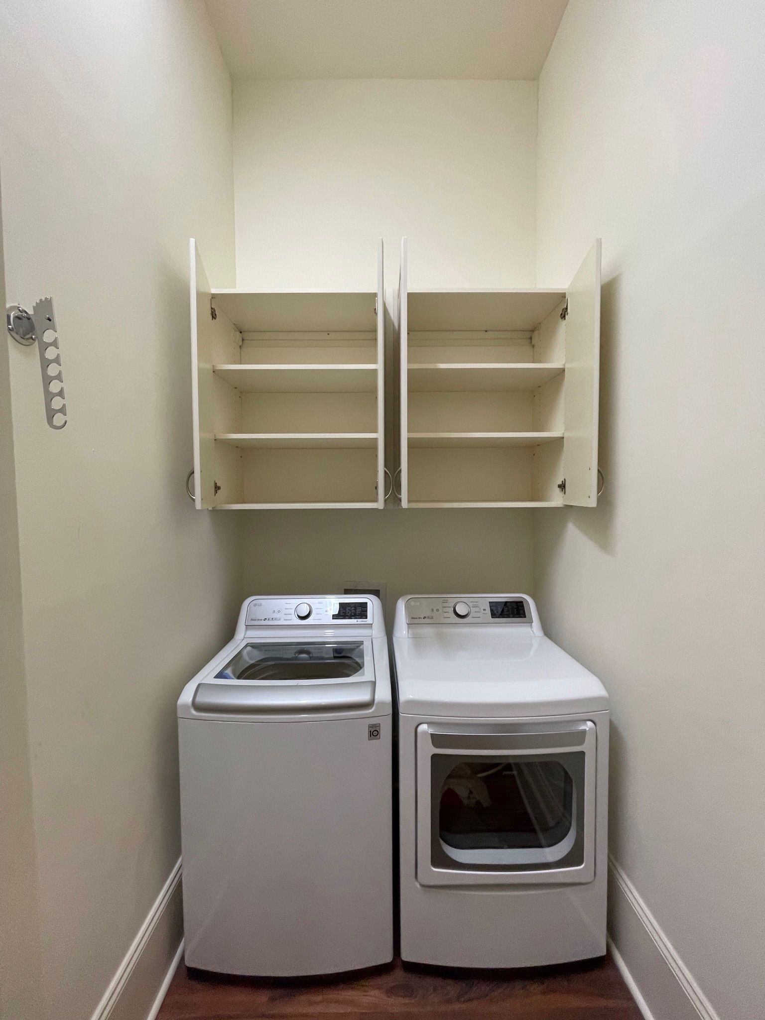 Laundry room with washer, dryer, and cabinets with open doors, all in neutral colors.
