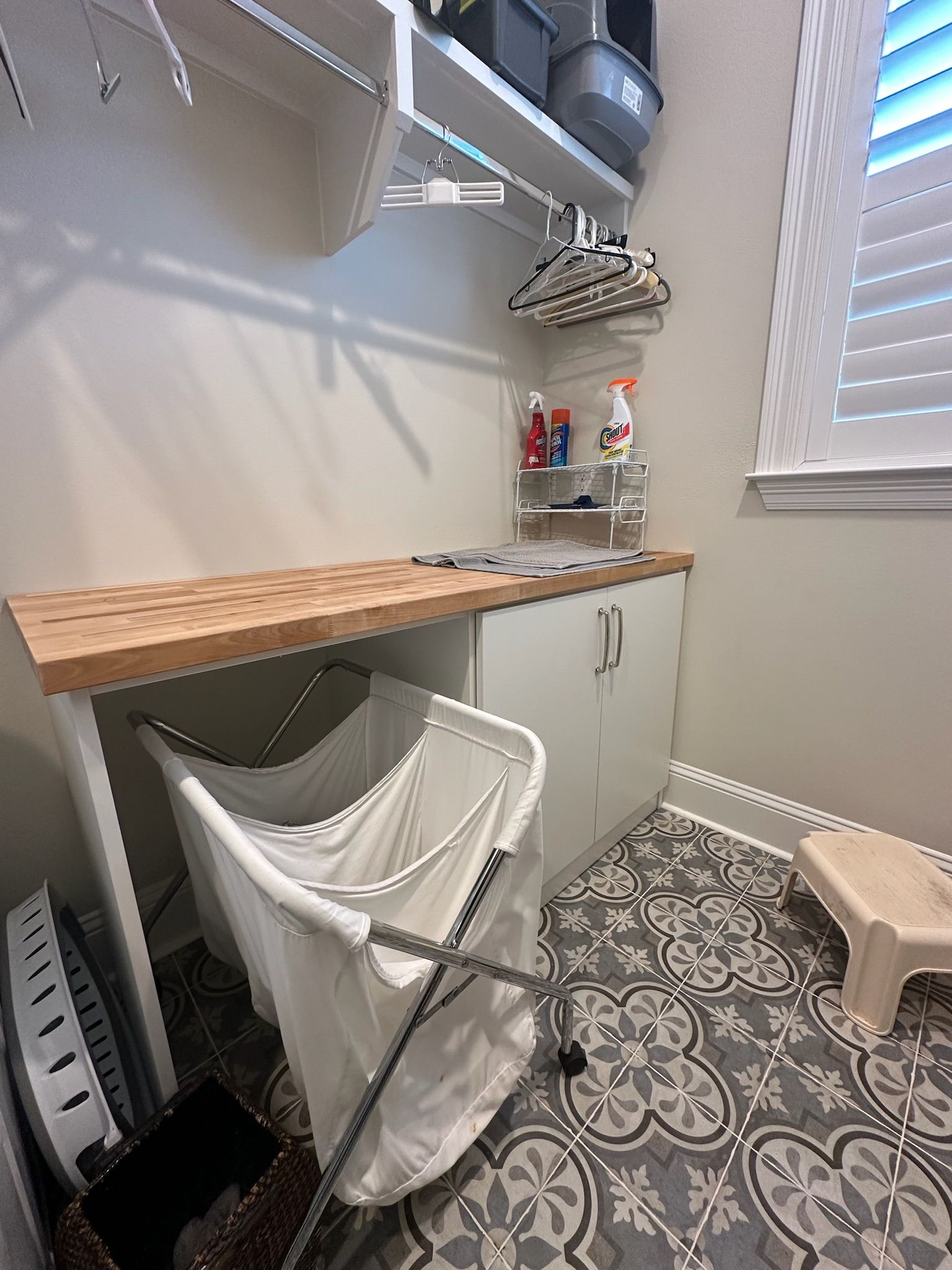 Laundry room with a countertop, storage, and a hamper. Gray and white patterned tile.