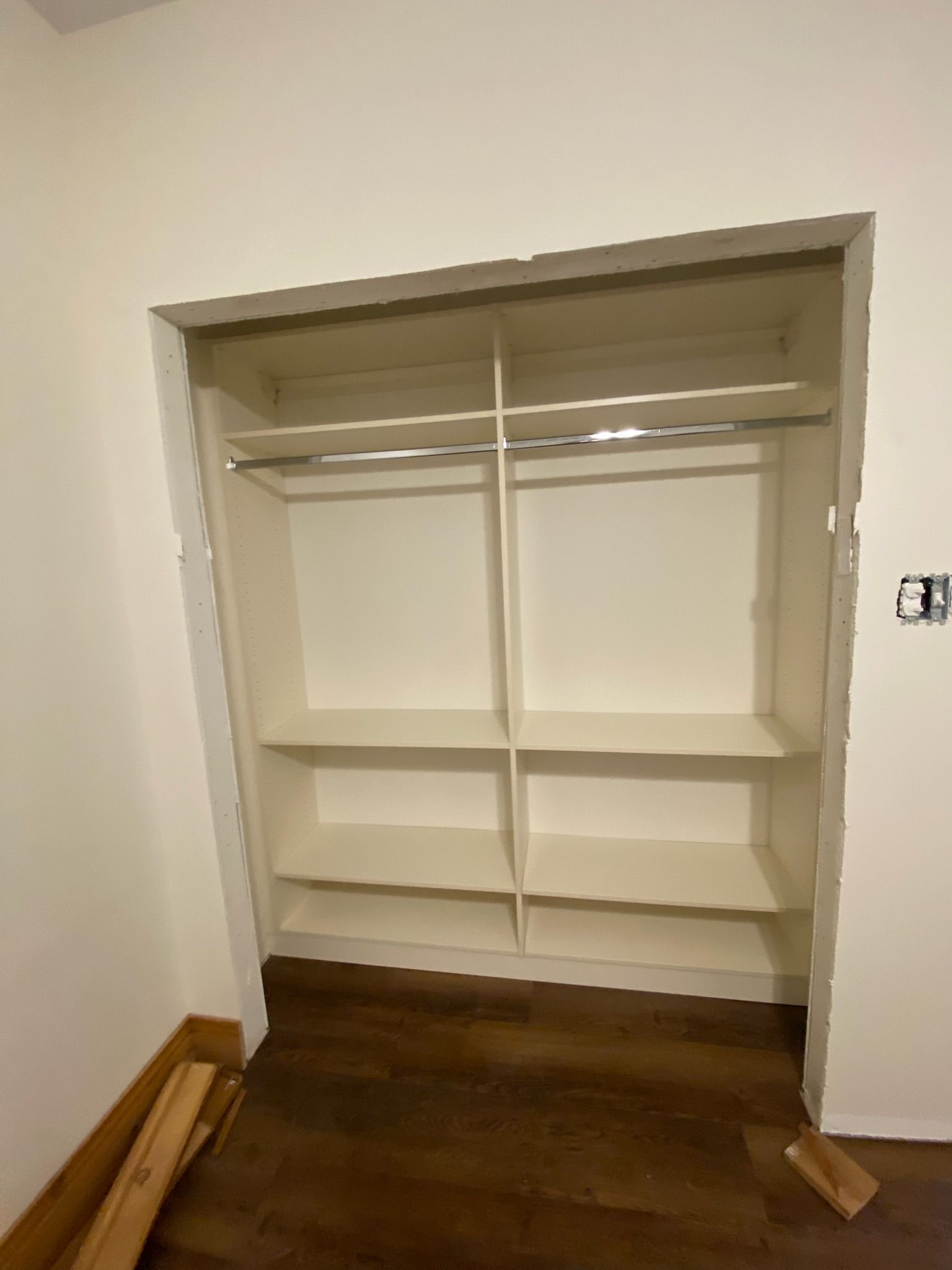 Built-in white closet with shelves and a clothing rod, set in a recessed wall, against a brown floor.