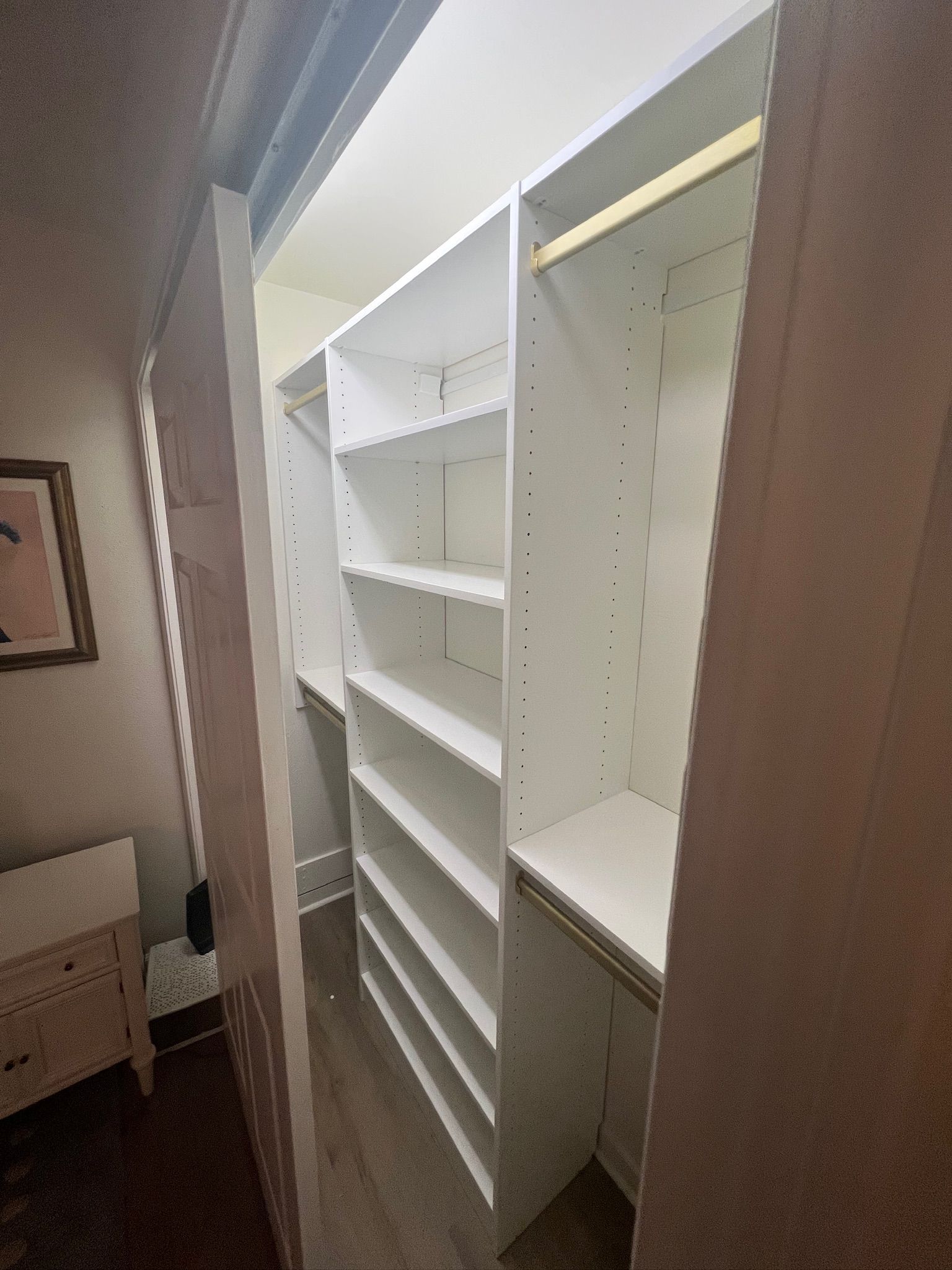 Walk-in closet with white shelves and clothing rods. Doorway on the right. Dark wood floor.