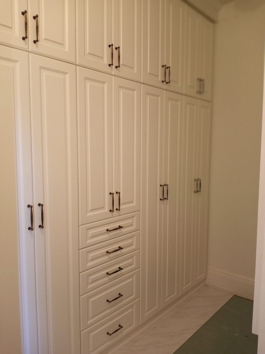 White built-in closet with multiple doors and drawers, dark hardware.
