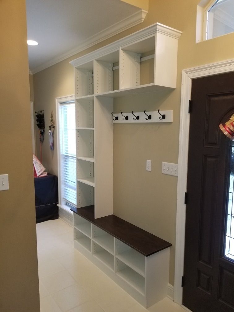 Built-in white entryway organizer with shelves, bench, hooks, and dark brown bench seat.
