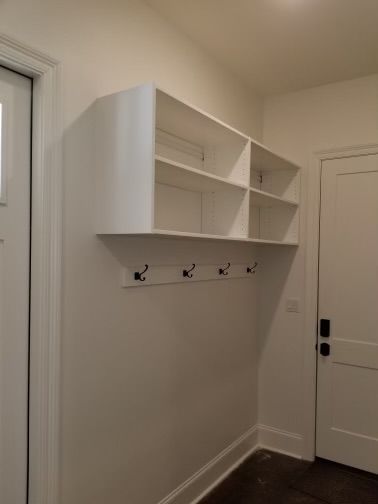 White built-in shelf unit with hooks on a wall. Doorways on either side.