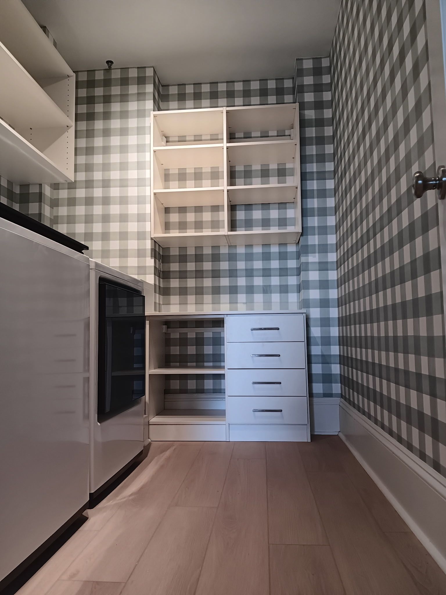 Small kitchen with light wood floor, white cabinetry, and checkered gray wallpaper.
