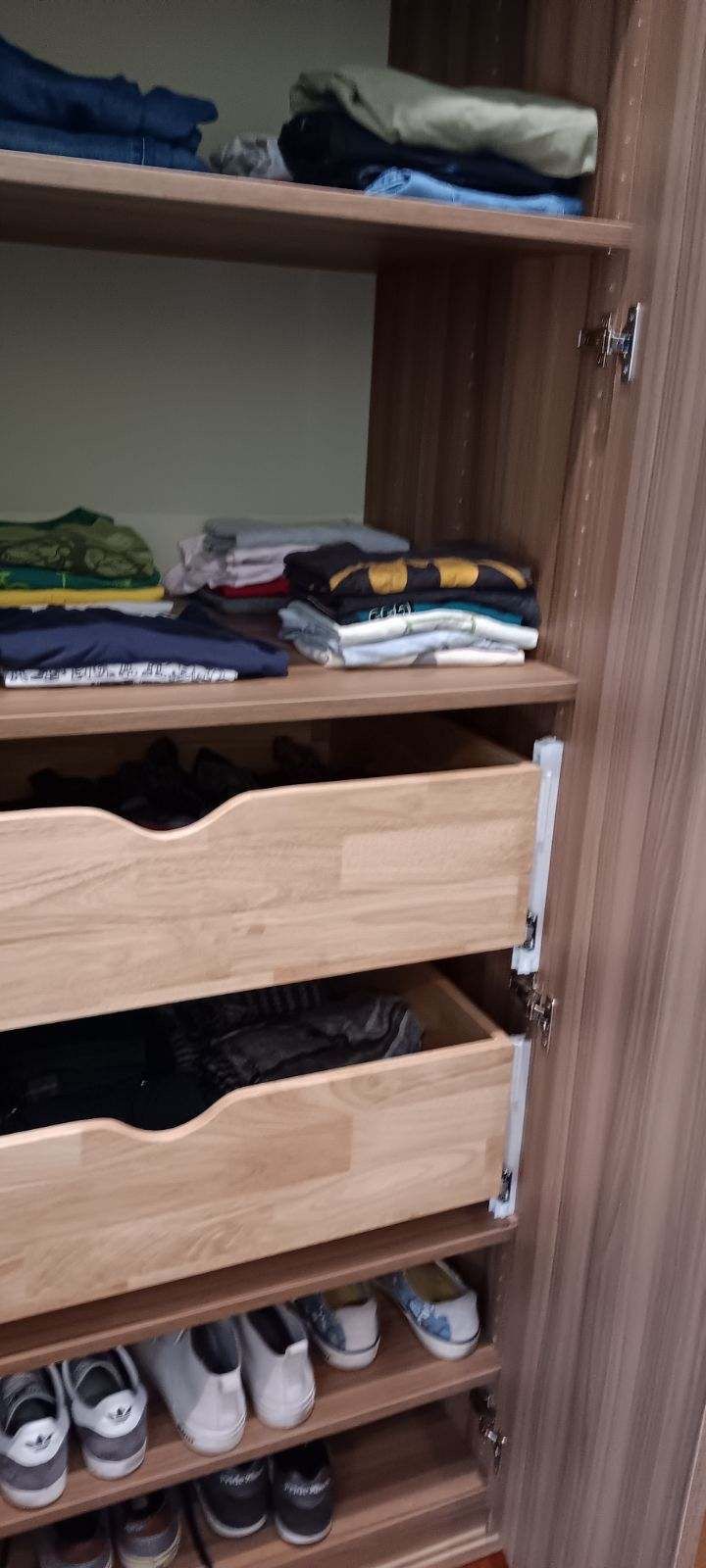 Wooden wardrobe with shelves of clothes, two open drawers, and a shoe rack at the bottom.