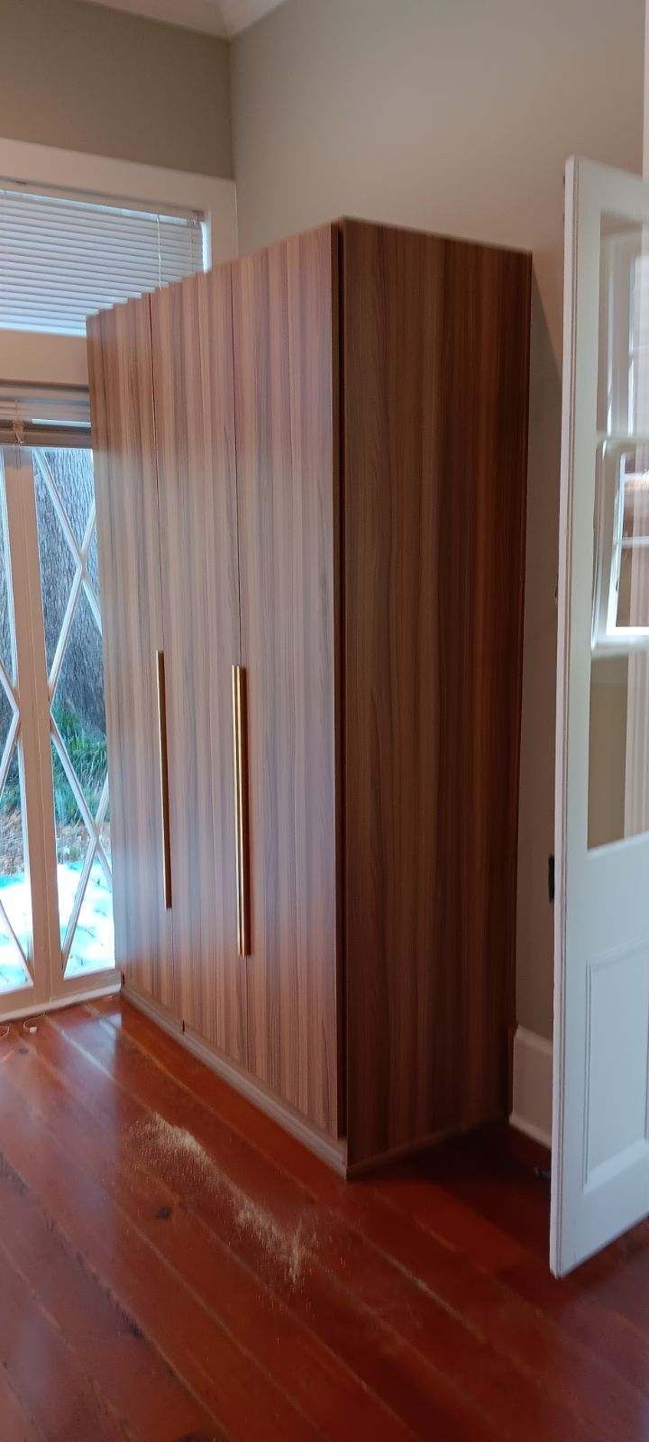 Wooden closet with gold handles in a room with hardwood floors and a white door.