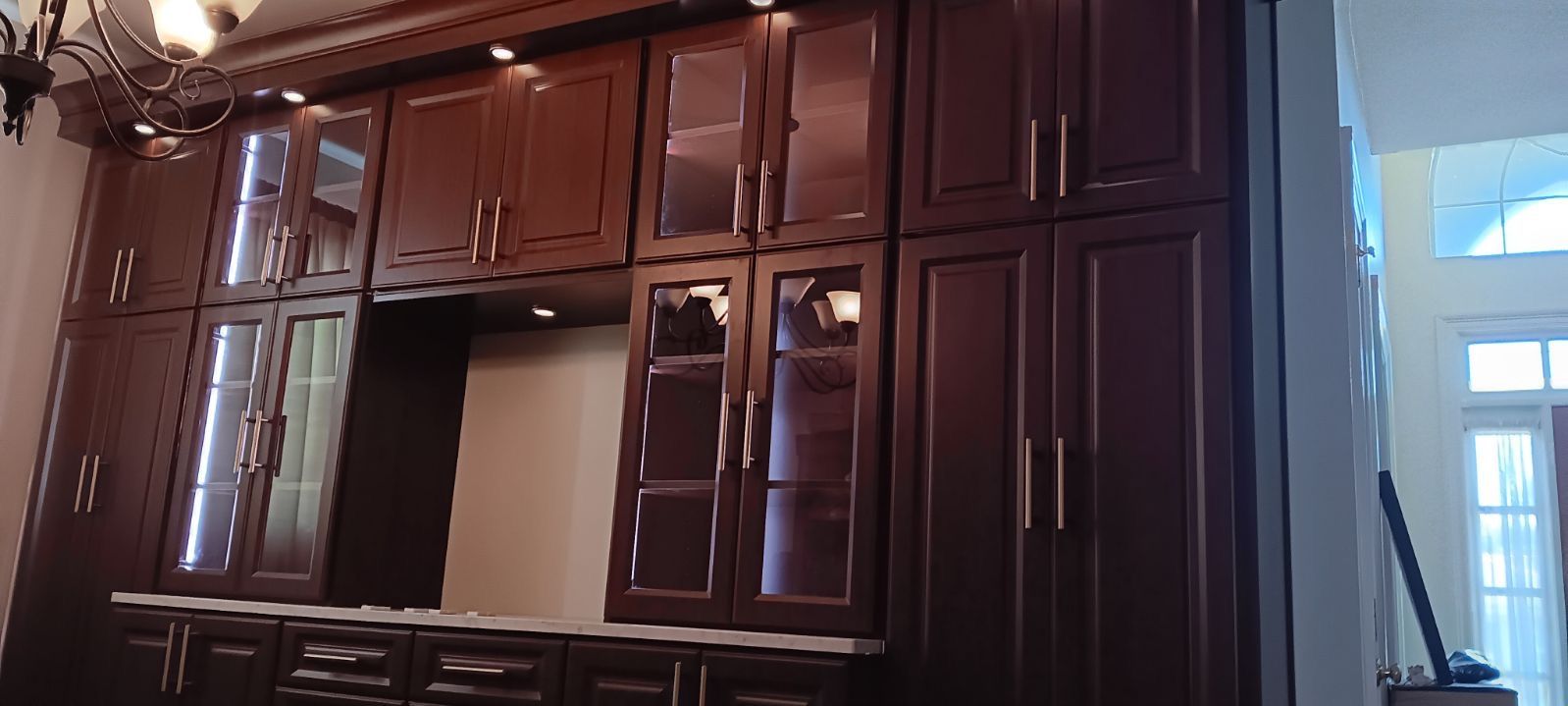 Dark wood cabinets with glass-fronted sections and a built-in space. A chandelier is visible.