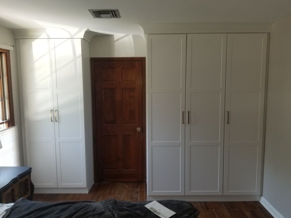 White built-in wardrobe with four doors next to a dark wood door in a room with hardwood floors.