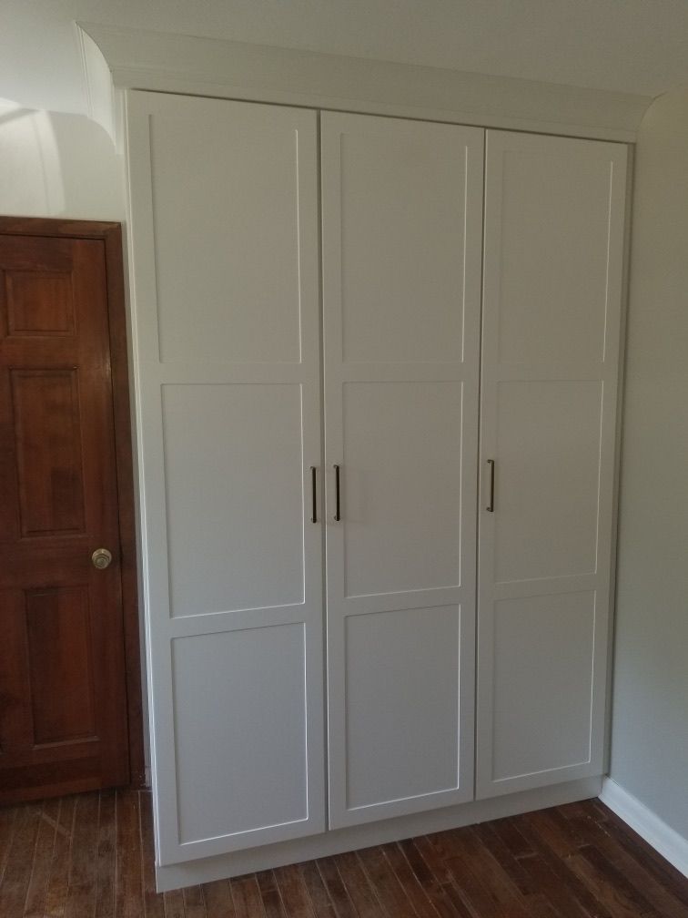 White built-in closet with three doors and black handles against a wall. Wooden door to the left.