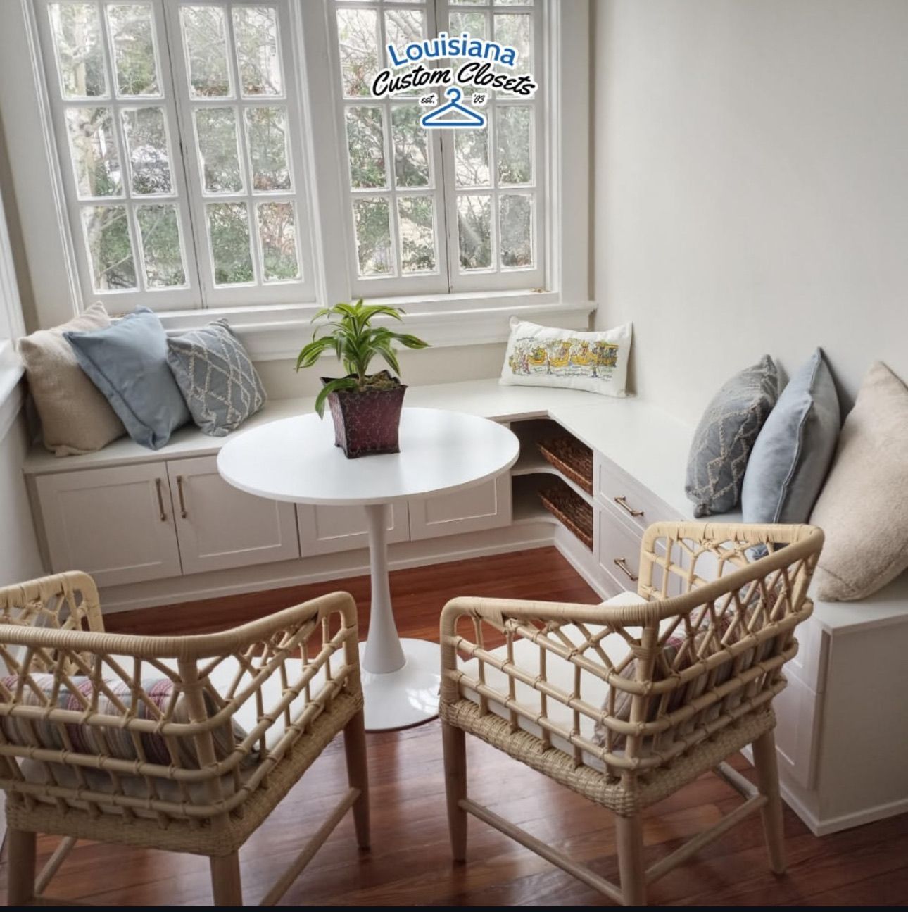 Cozy breakfast nook with white round table, built-in bench, wicker chairs, and window.