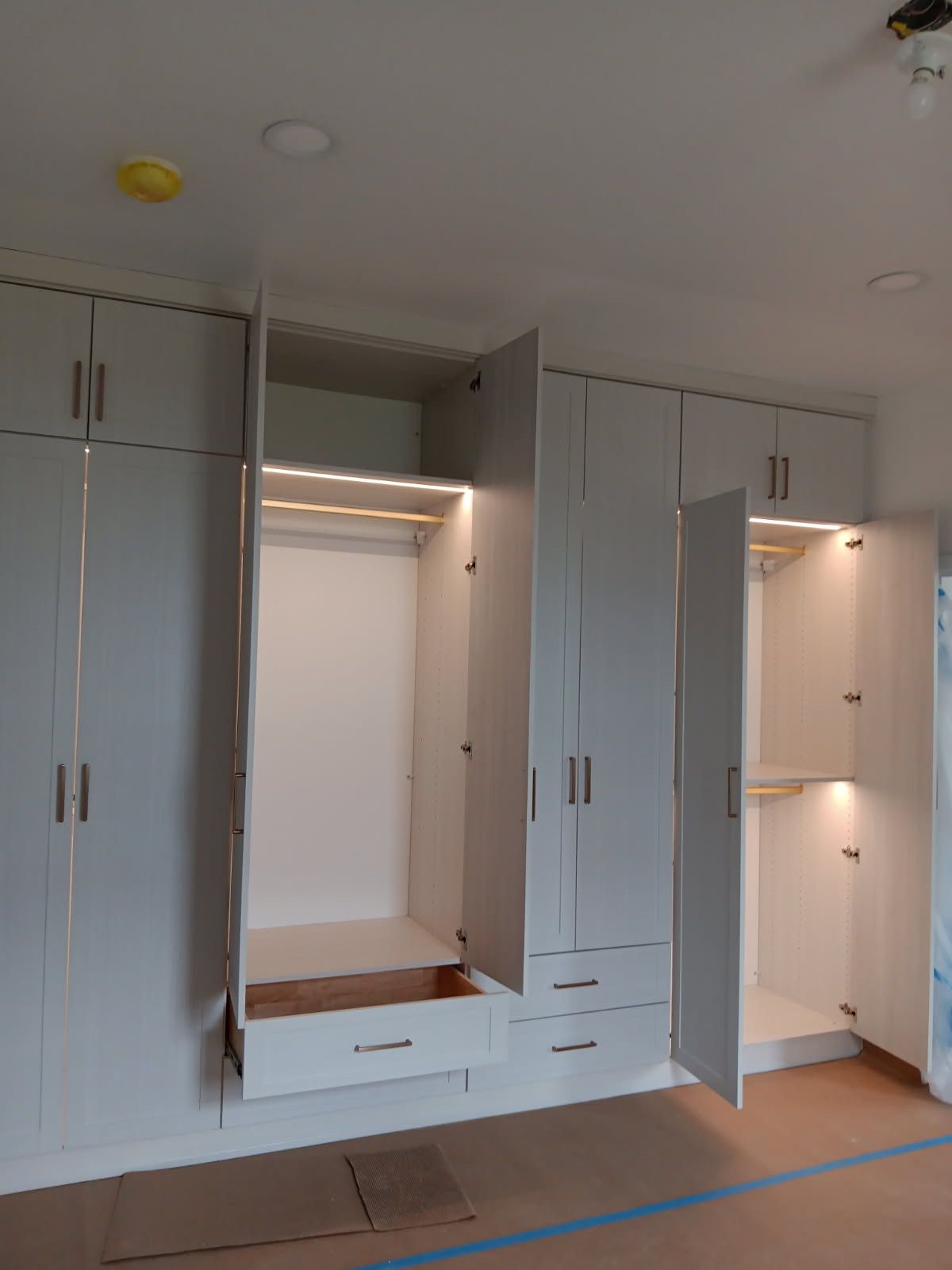 Built-in white cabinets with open doors, hanging rods, drawers, and interior lighting in a room.