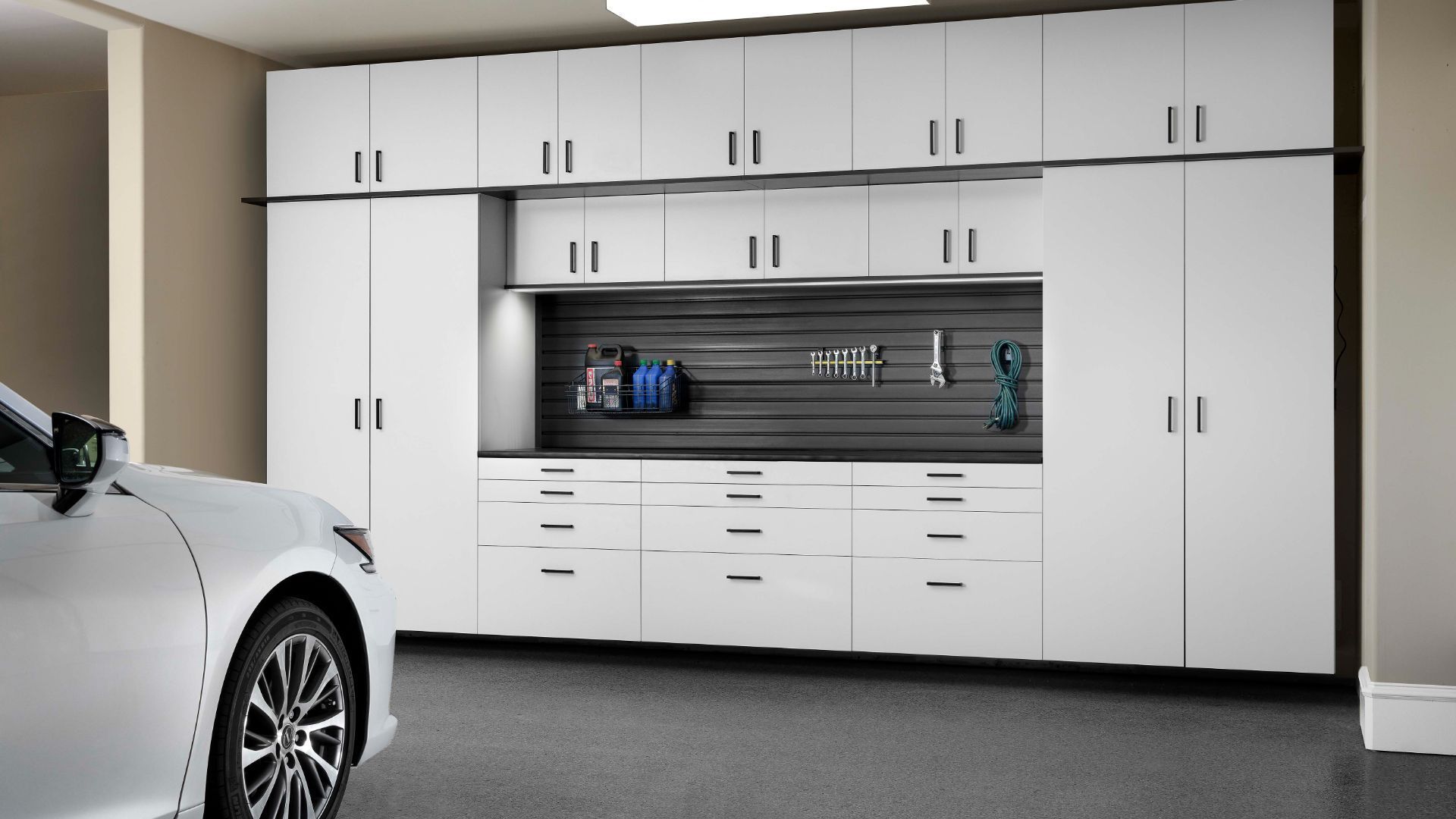 White car parked next to garage storage cabinets, organized with tools and drawers.