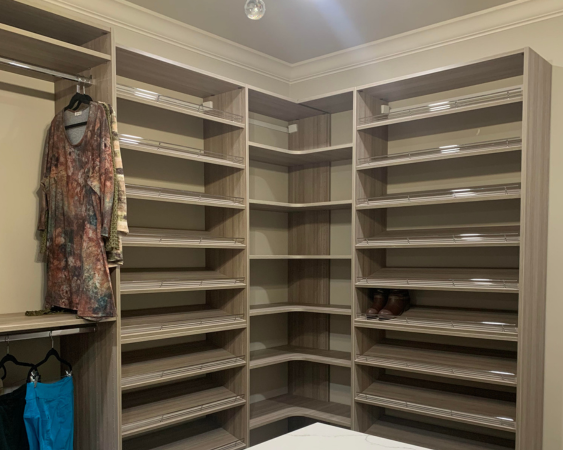 Closet with built-in shelves and hanging rod. Light brown wood, empty shelves, some hanging clothes.