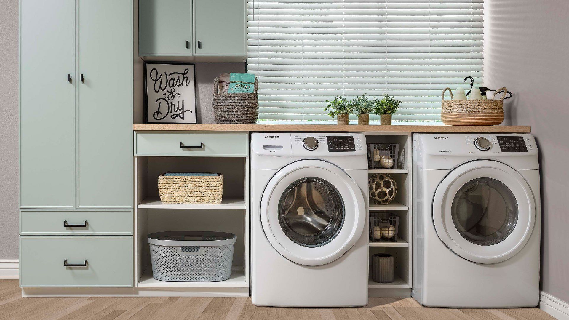 Laundry room with light green cabinets, white appliances, and wicker baskets.