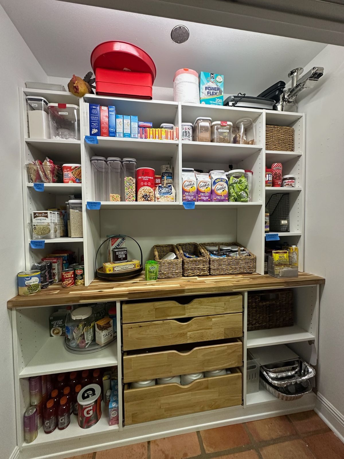 White pantry with shelves, drawers, and various food items, including snacks and drinks, inside.