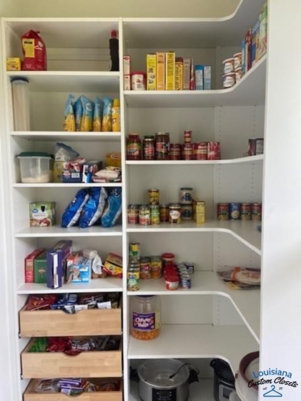 White pantry filled with organized food items on shelves and in drawers.