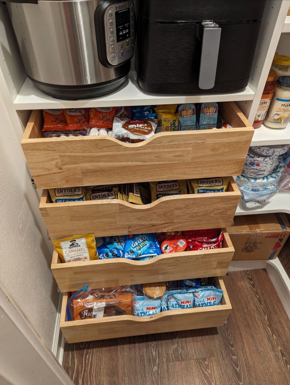 Wooden drawers in pantry filled with snacks and food items, with an Instant Pot and air fryer on top.