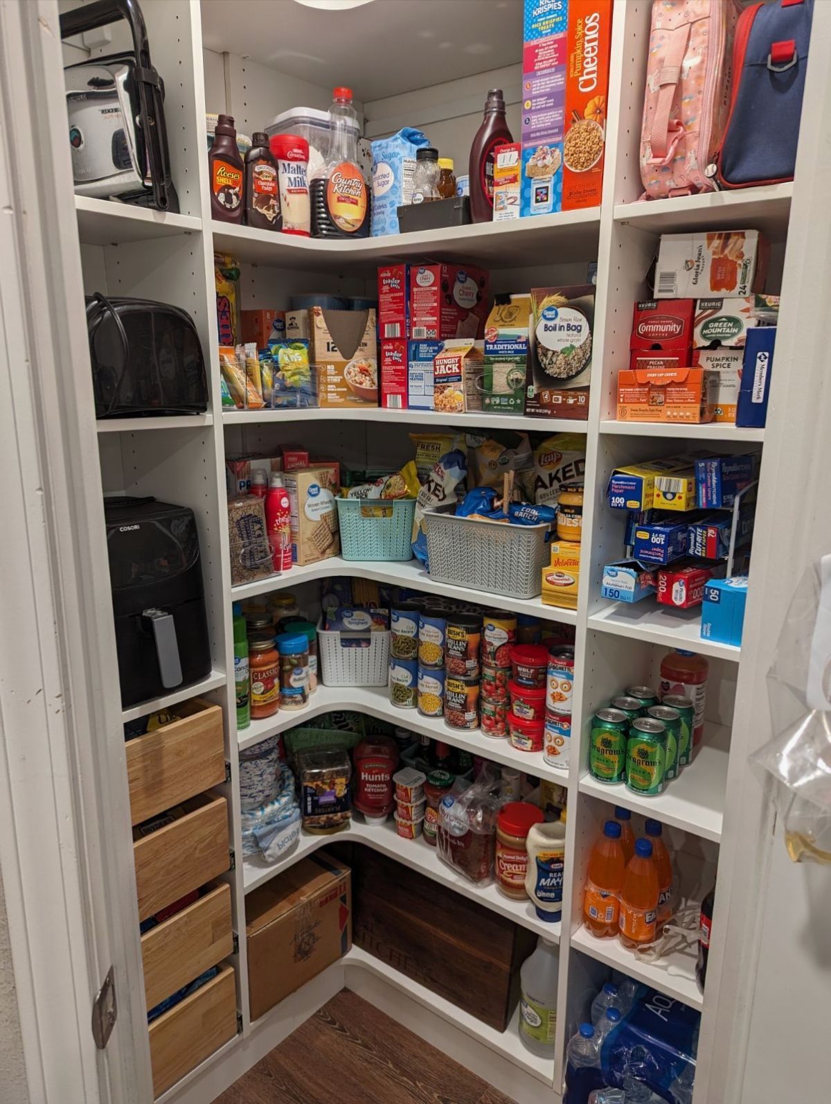 A well-stocked pantry with white shelves containing various food items.