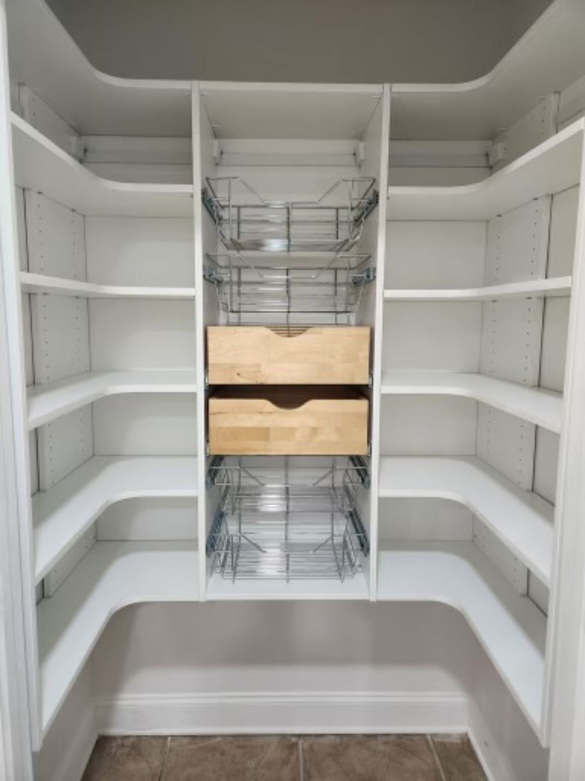 White pantry with curved shelves and wire baskets, wooden drawers.