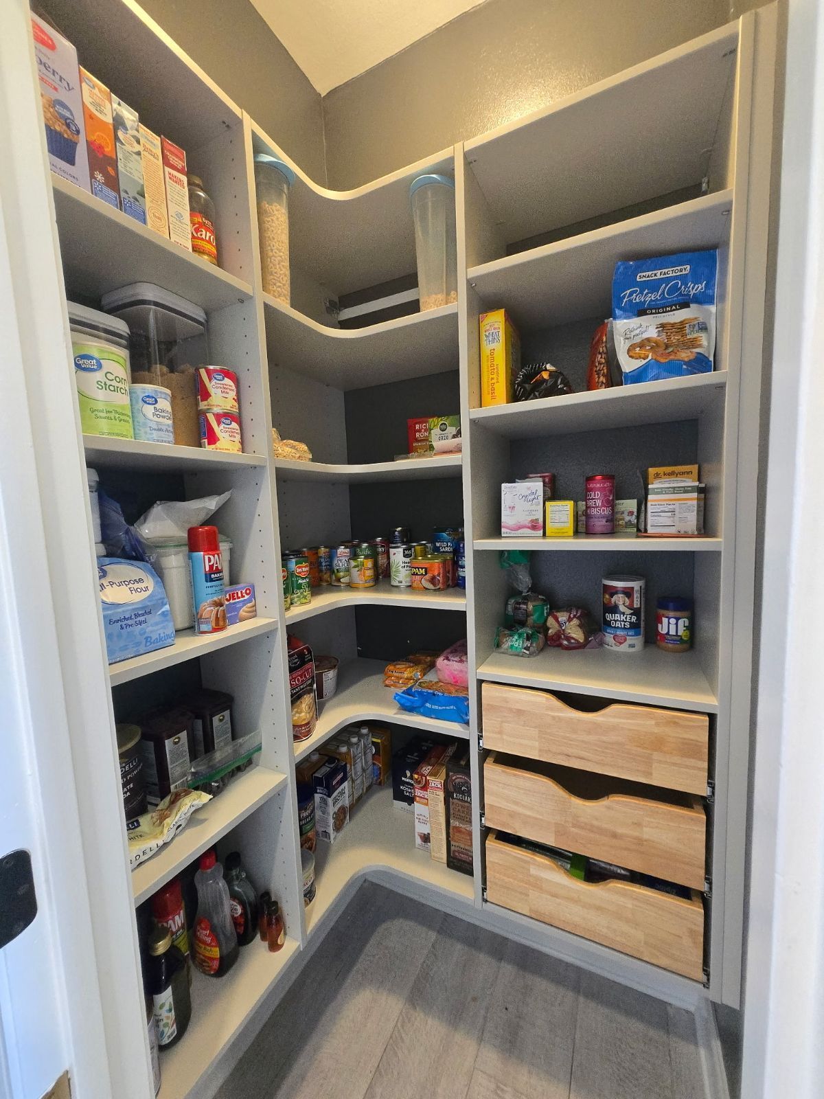 A well-organized pantry with light shelves, various food items, and wooden drawers.