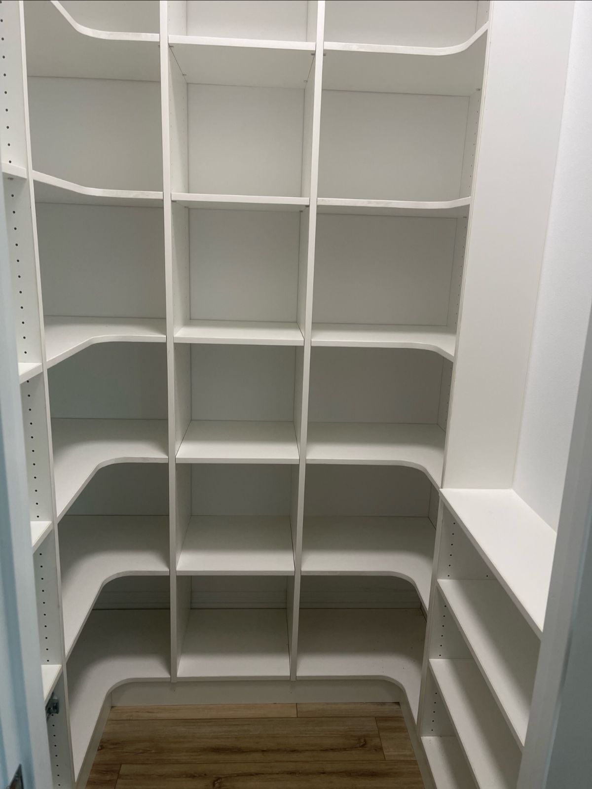 White built-in shelves with multiple compartments in a walk-in closet with wood flooring.