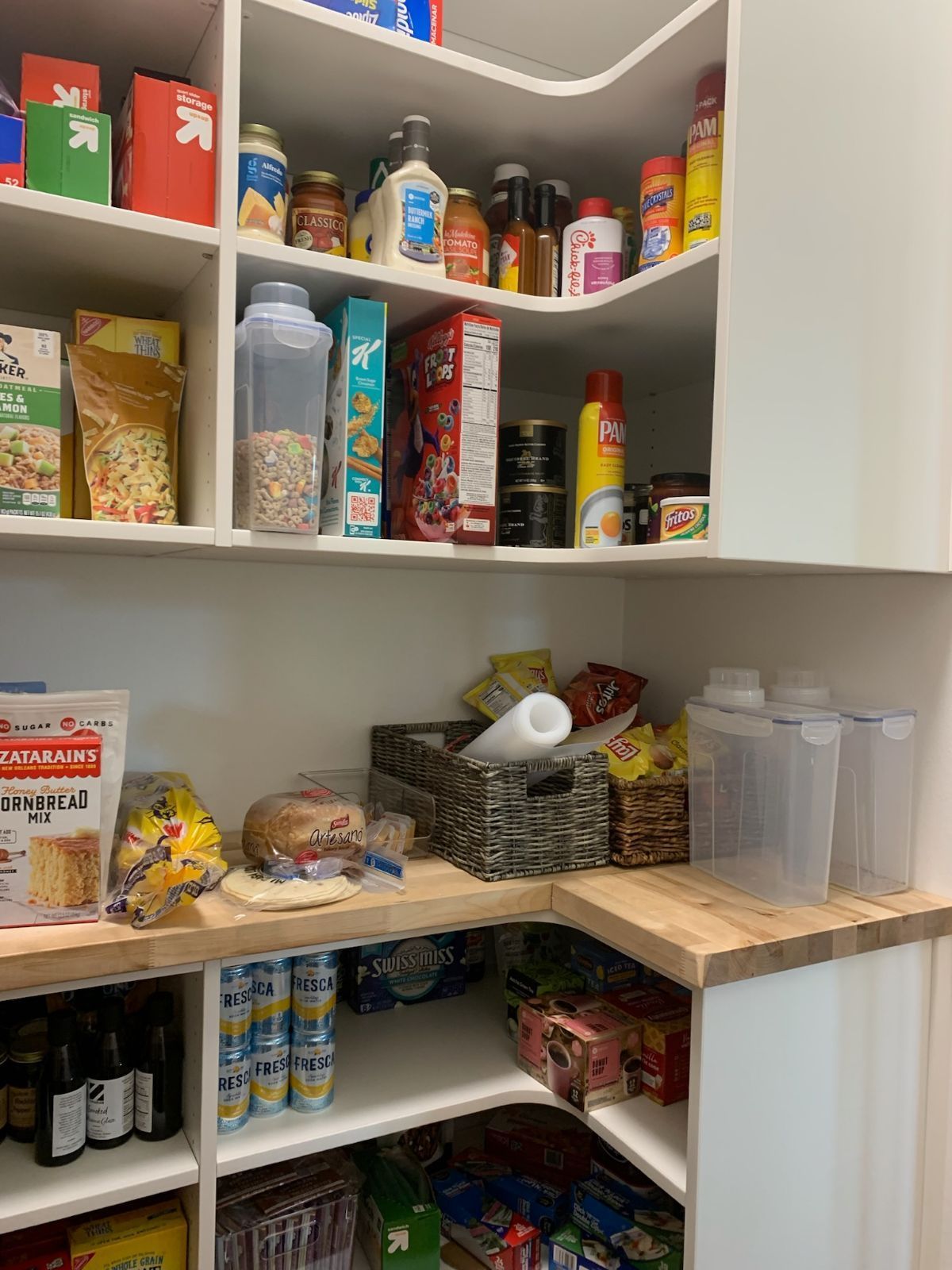 Pantry with white shelves holding various food items. Angled corner with wood countertop and baskets.