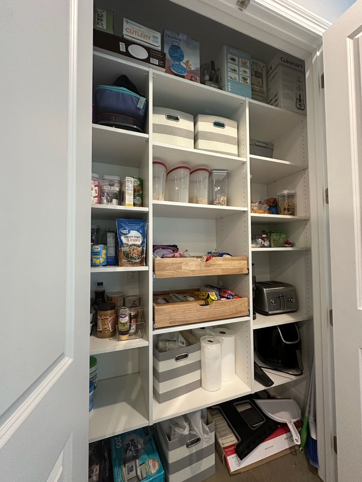 White pantry with shelves holding food, appliances, and containers.