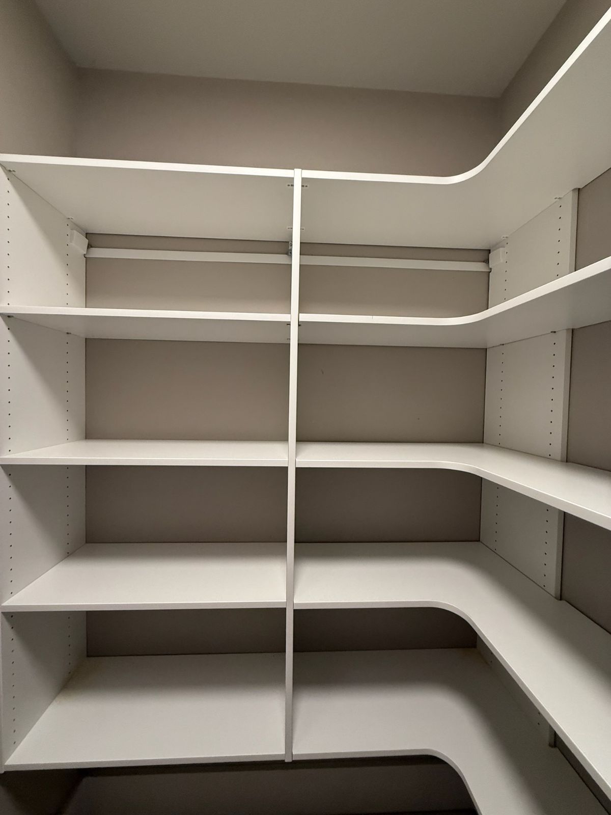White built-in shelving unit in a closet. Shelves are empty, with a corner design.