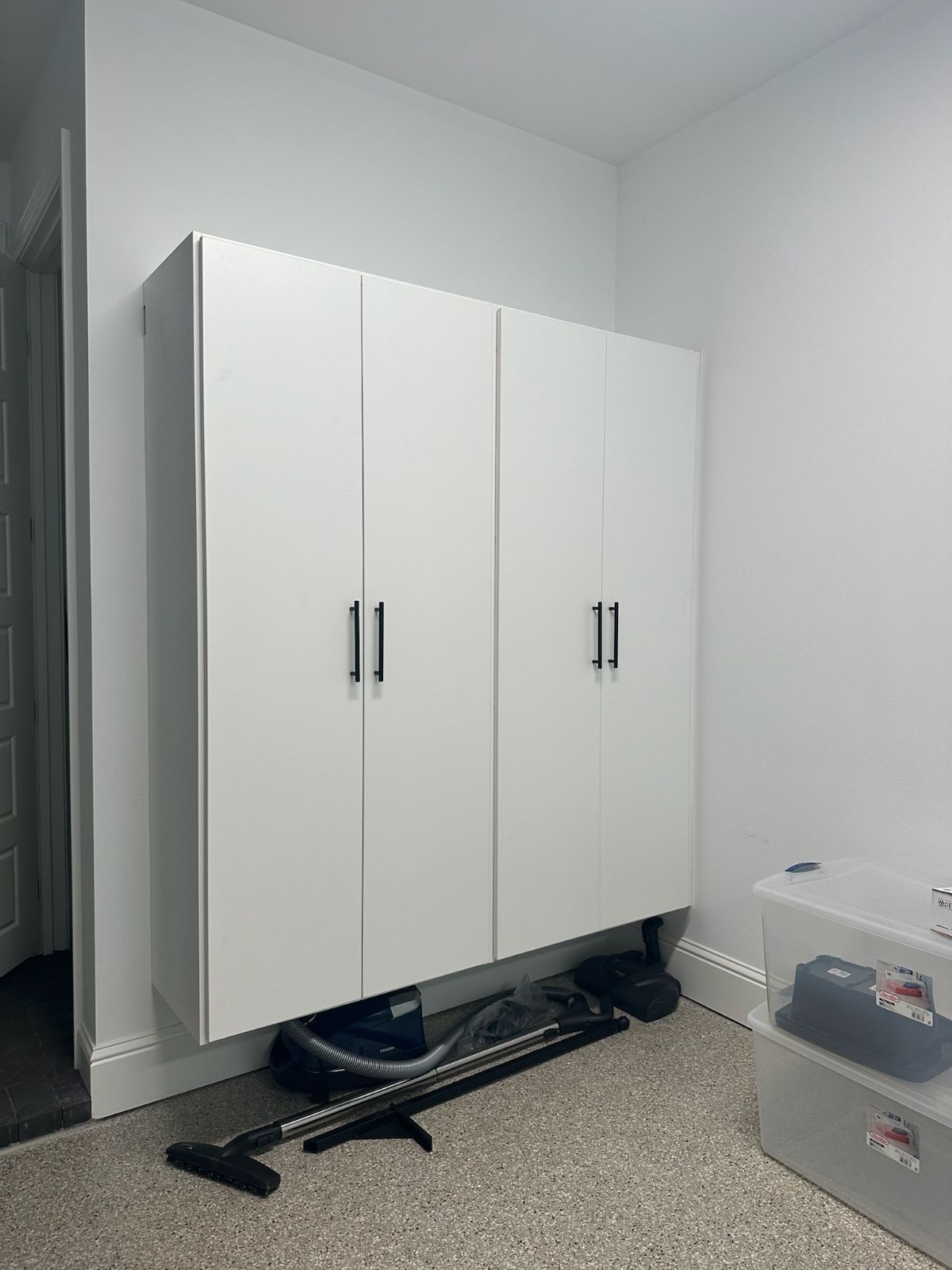 White storage cabinets mounted on a wall. A vacuum cleaner and other items are below.