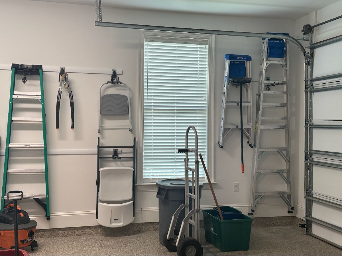 Garage interior with tools, ladders, and a hand truck; a window with blinds is centered.
