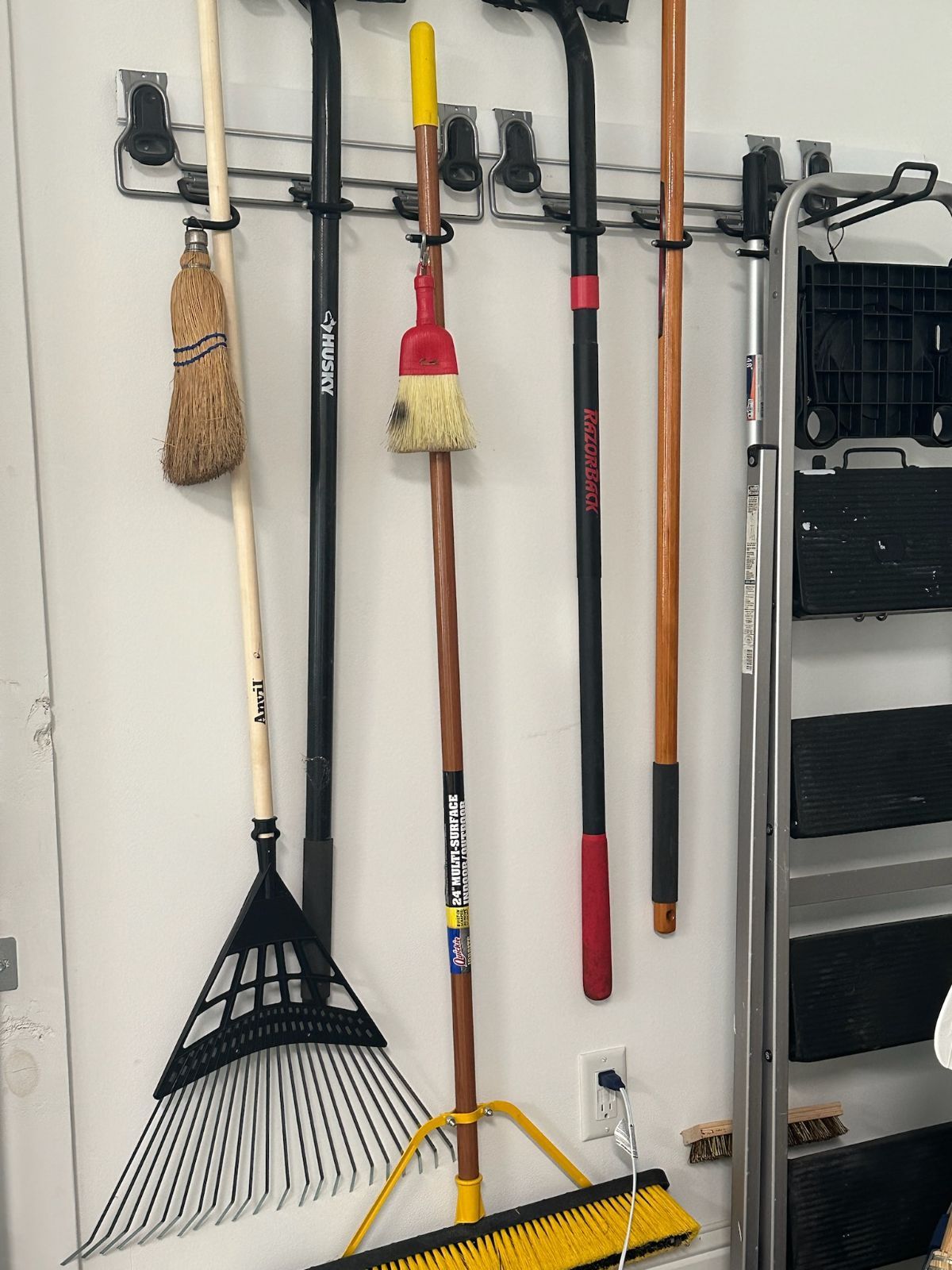 Gardening tools hanging on a wall-mounted rack: broom, rake, and other long-handled tools.