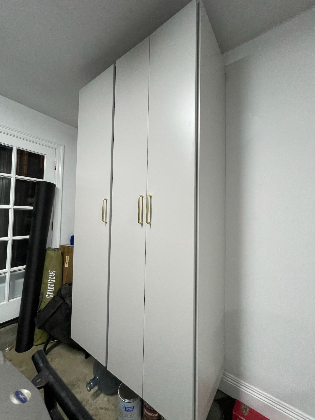White storage cabinets with gold handles in a garage, next to a white wall.