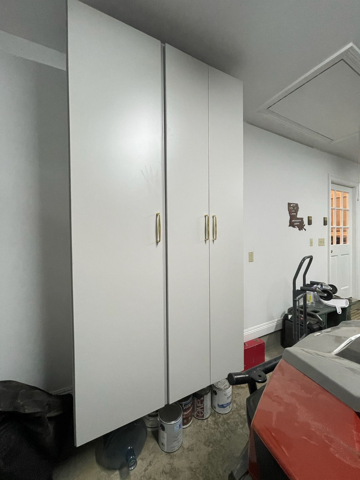 Tall white storage cabinets in a garage; a red object and equipment are in the foreground.