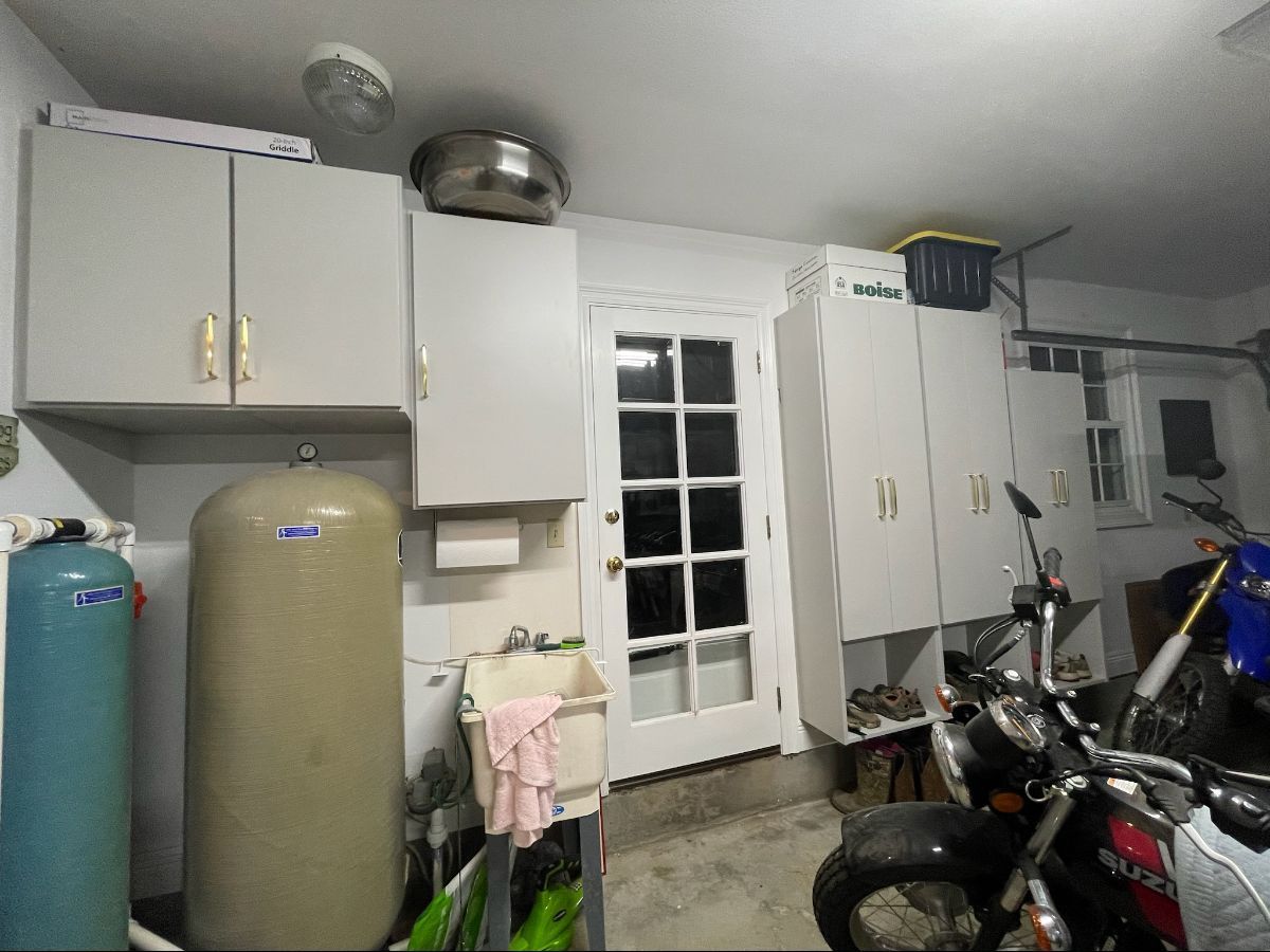 Garage interior with cabinets, water tank, door, and motorcycle.