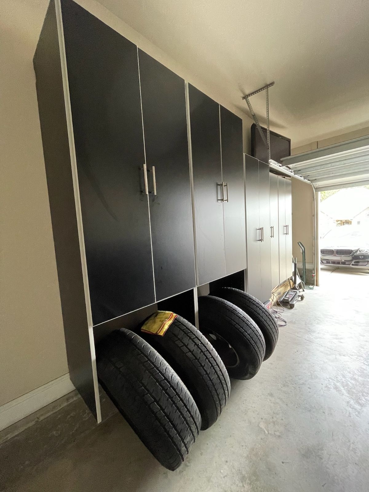 Garage cabinets, black and gray, with tires stored beneath.
