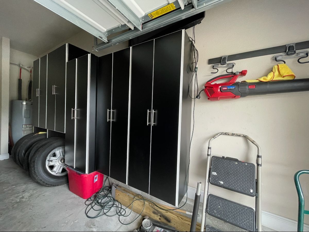 Garage storage: Black cabinets, tires, red bin, ladder, and a leaf blower.
