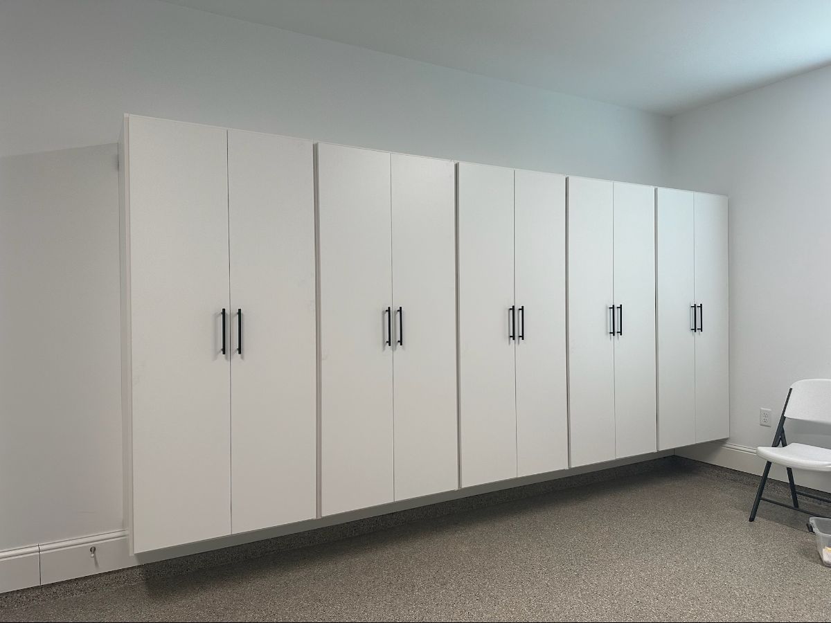 White wall-mounted cabinets with black handles, set against a neutral wall and carpeted floor.