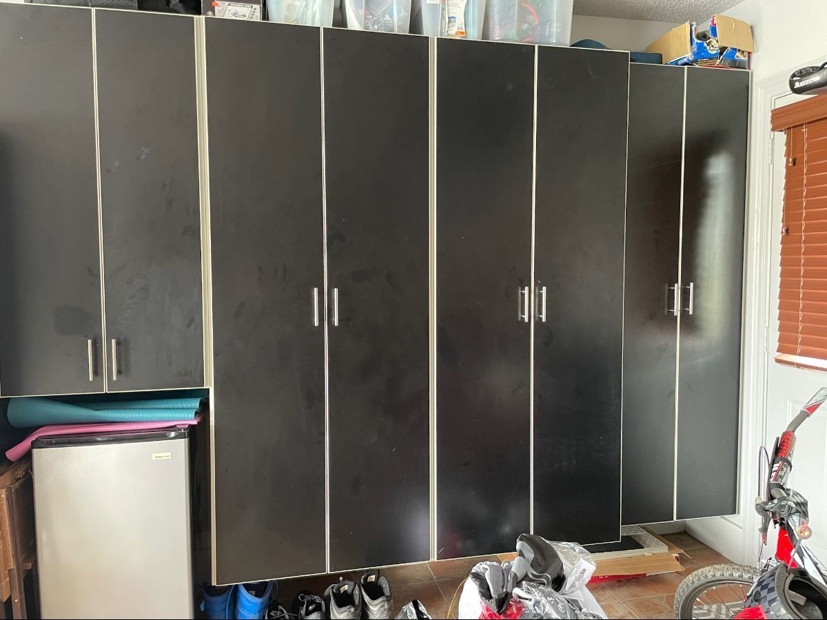Dark cabinets and a small refrigerator in a garage setting with some clutter.