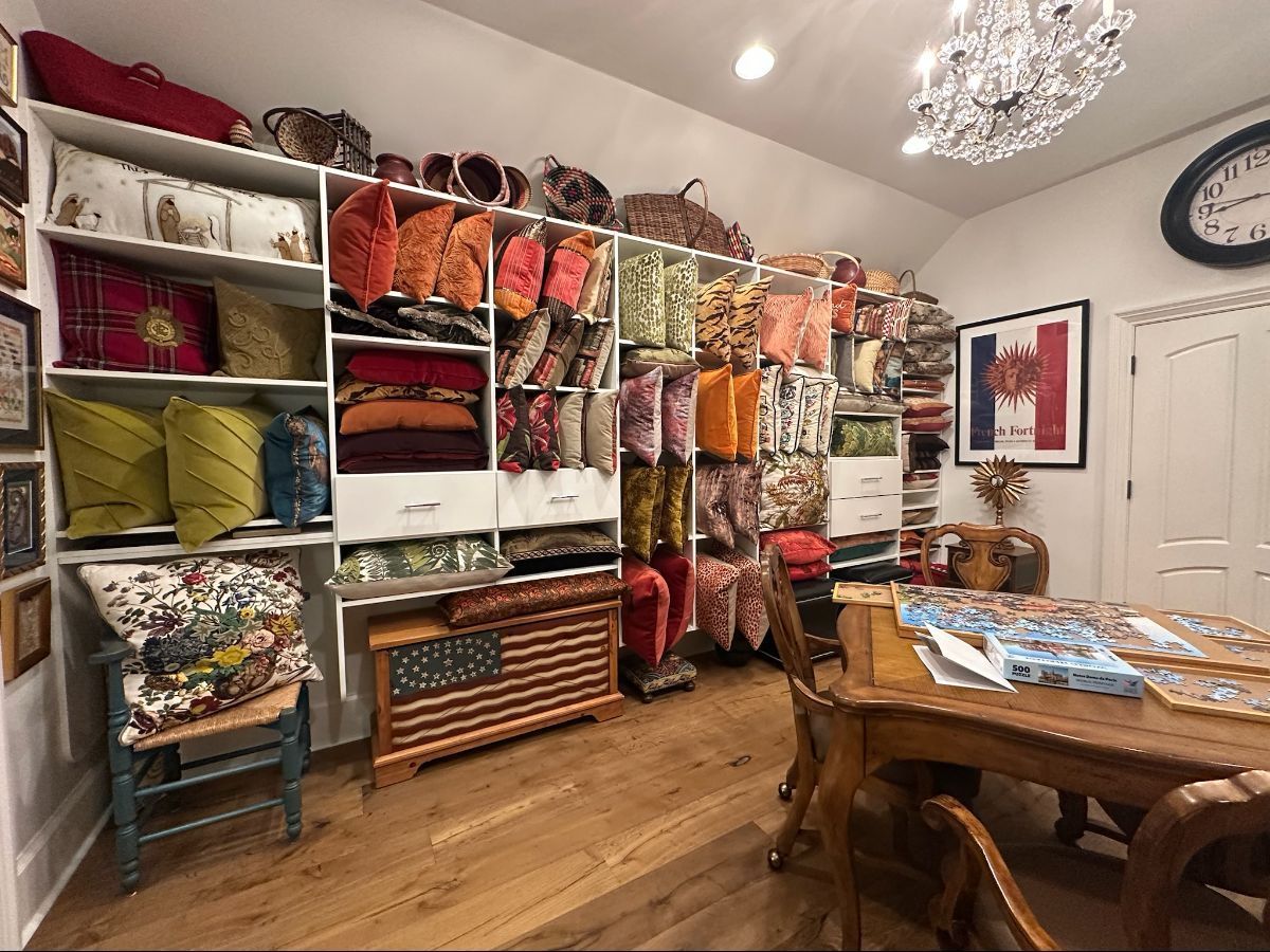 A room filled with pillows and fabrics on shelves, a table, and an American flag storage cabinet.