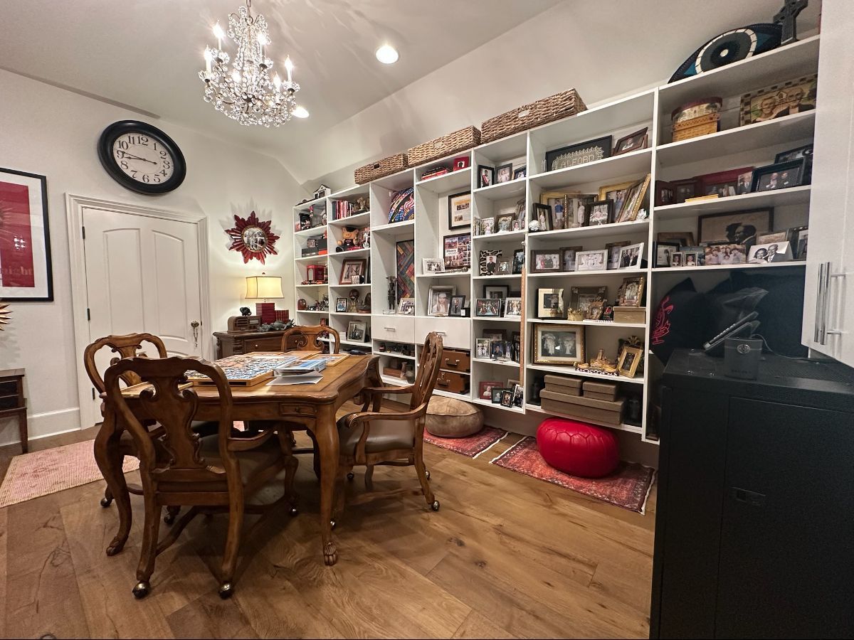 Dining room with wooden table, ornate chairs, large bookshelves filled with photos, and a chandelier.