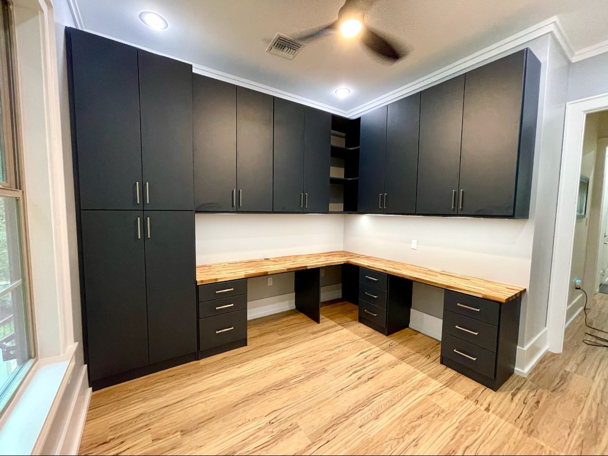 Black cabinets and desk in a corner office with a wooden countertop. The room has a beige floor and white walls.