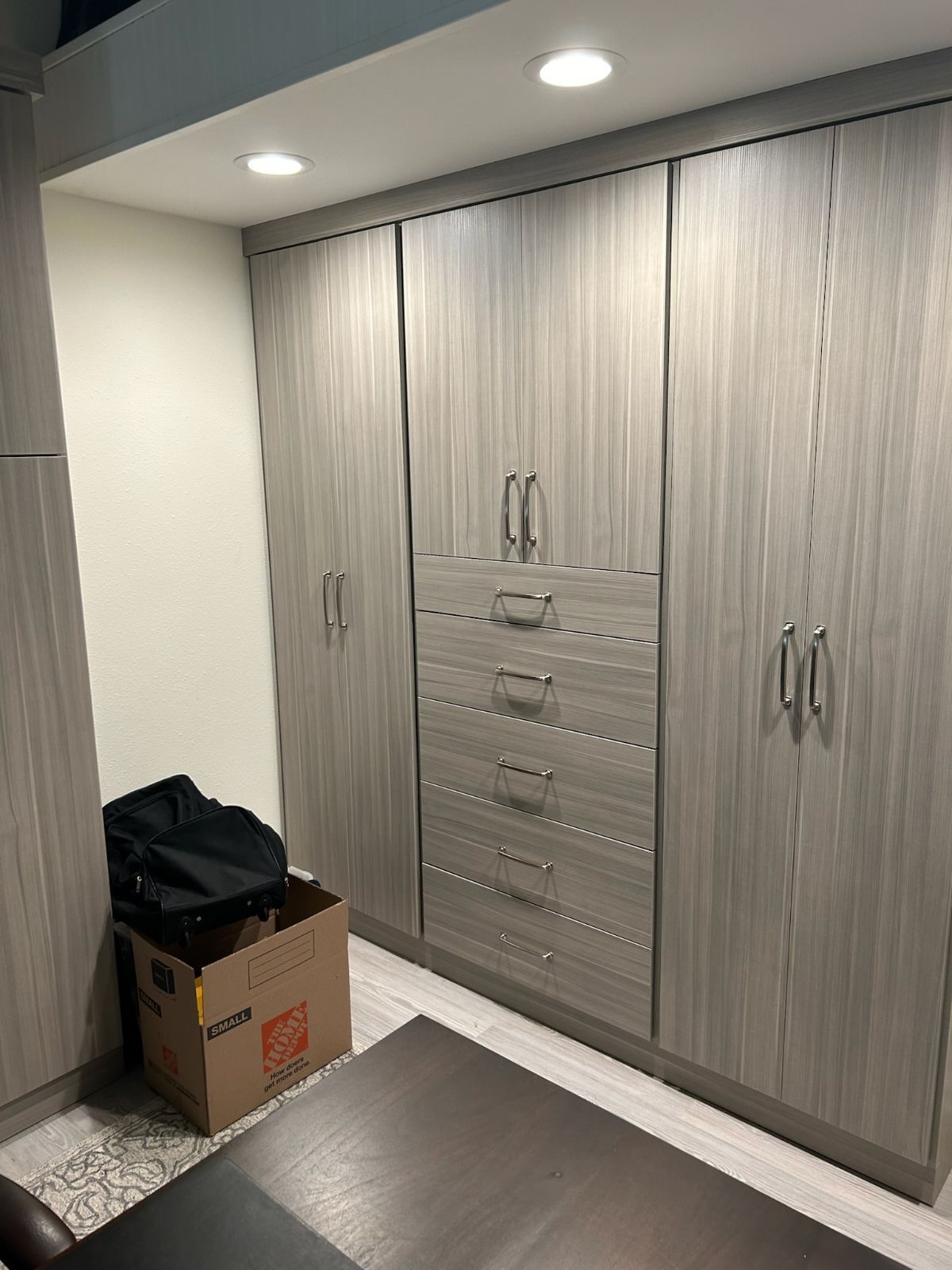 Built-in gray wood cabinets with silver hardware and a chest of drawers. A box and bag sit on the floor.