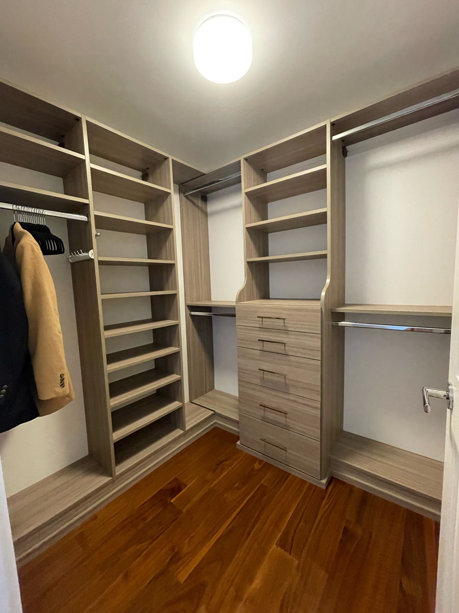 Walk-in closet with wooden shelves, rods, and drawers. Hardwood floor. Neutral color scheme.
