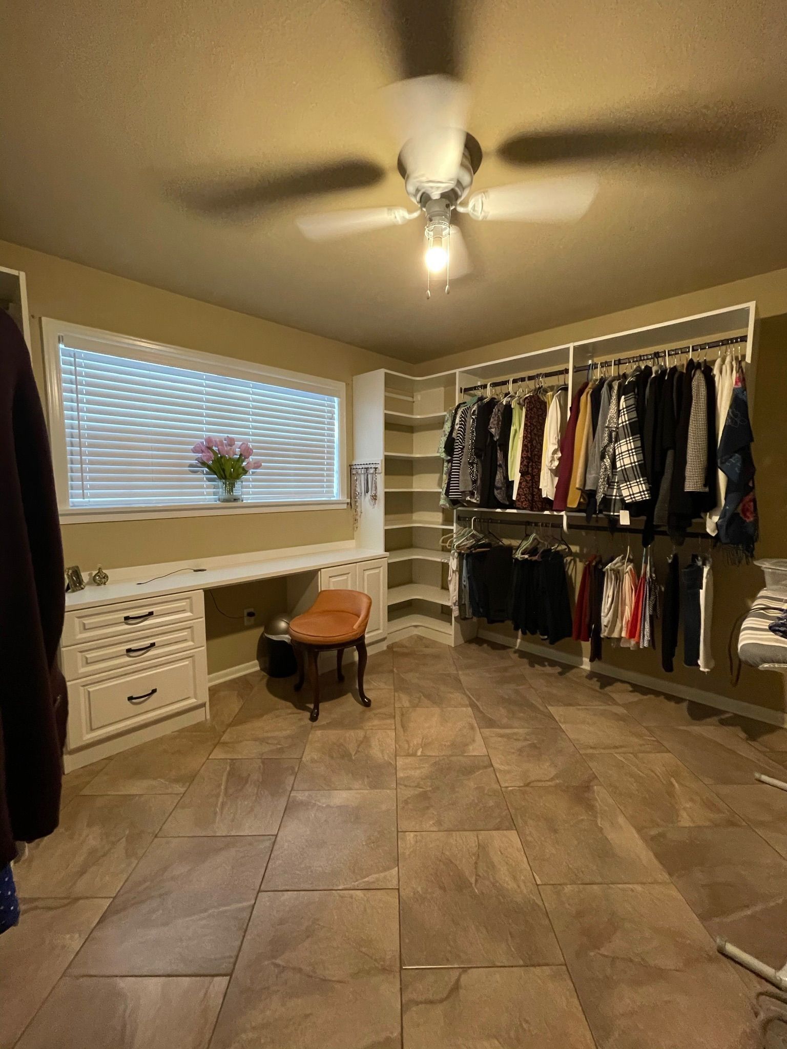Walk-in closet with clothes racks, a built-in desk, shelving, a ceiling fan, and tiled floor.