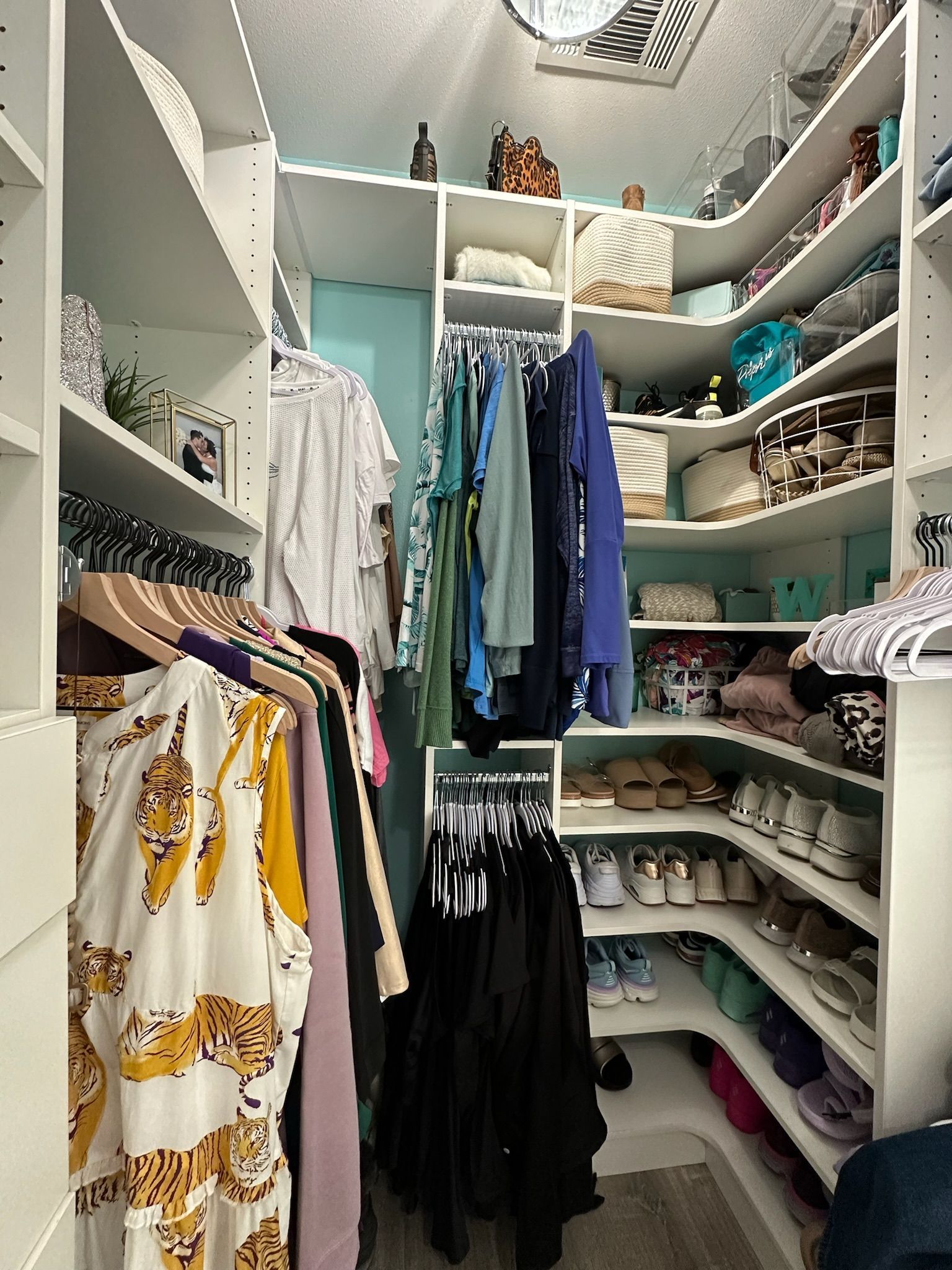 Walk-in closet with white shelves and various clothing items and accessories neatly arranged.