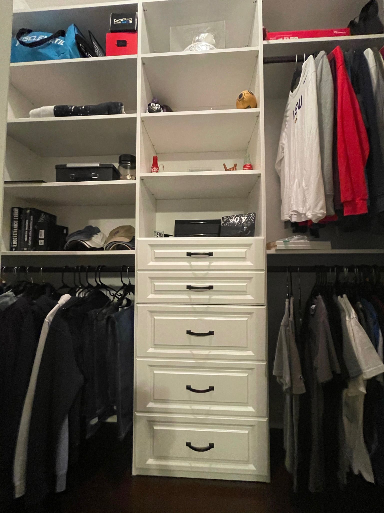 White closet organizer with shelves, drawers, and hanging rods filled with clothes and accessories.