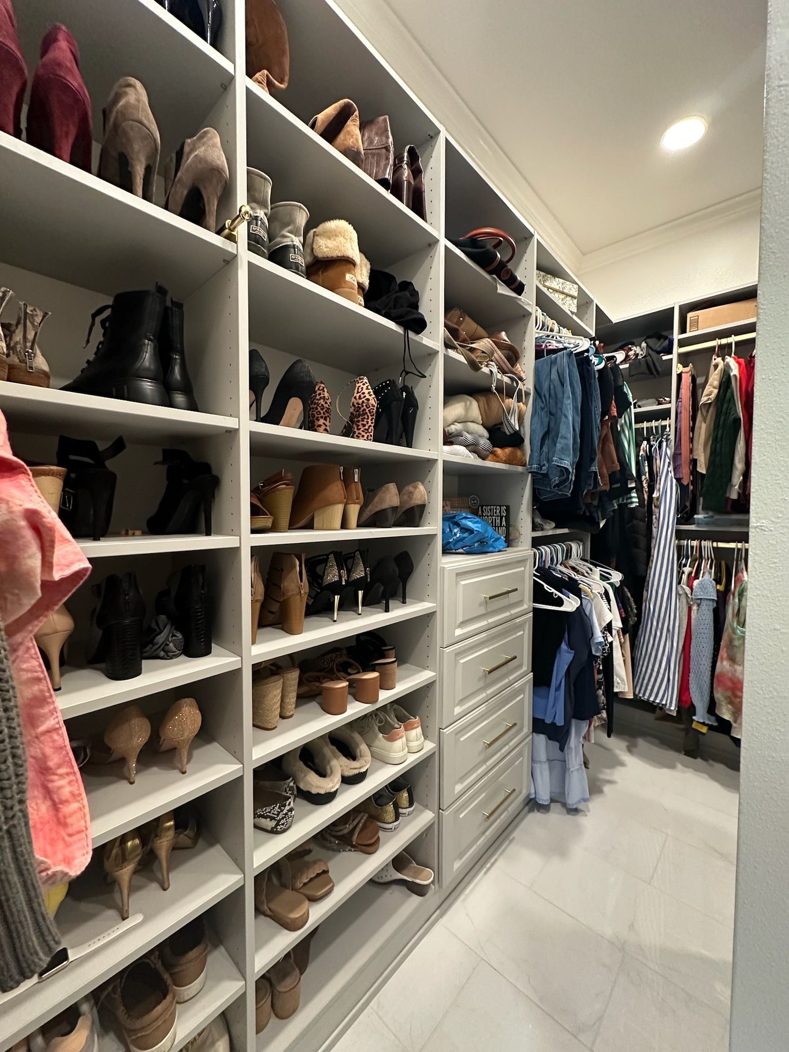 Walk-in closet with shelves filled with shoes and hanging clothes. Gray shelving, neutral tones.