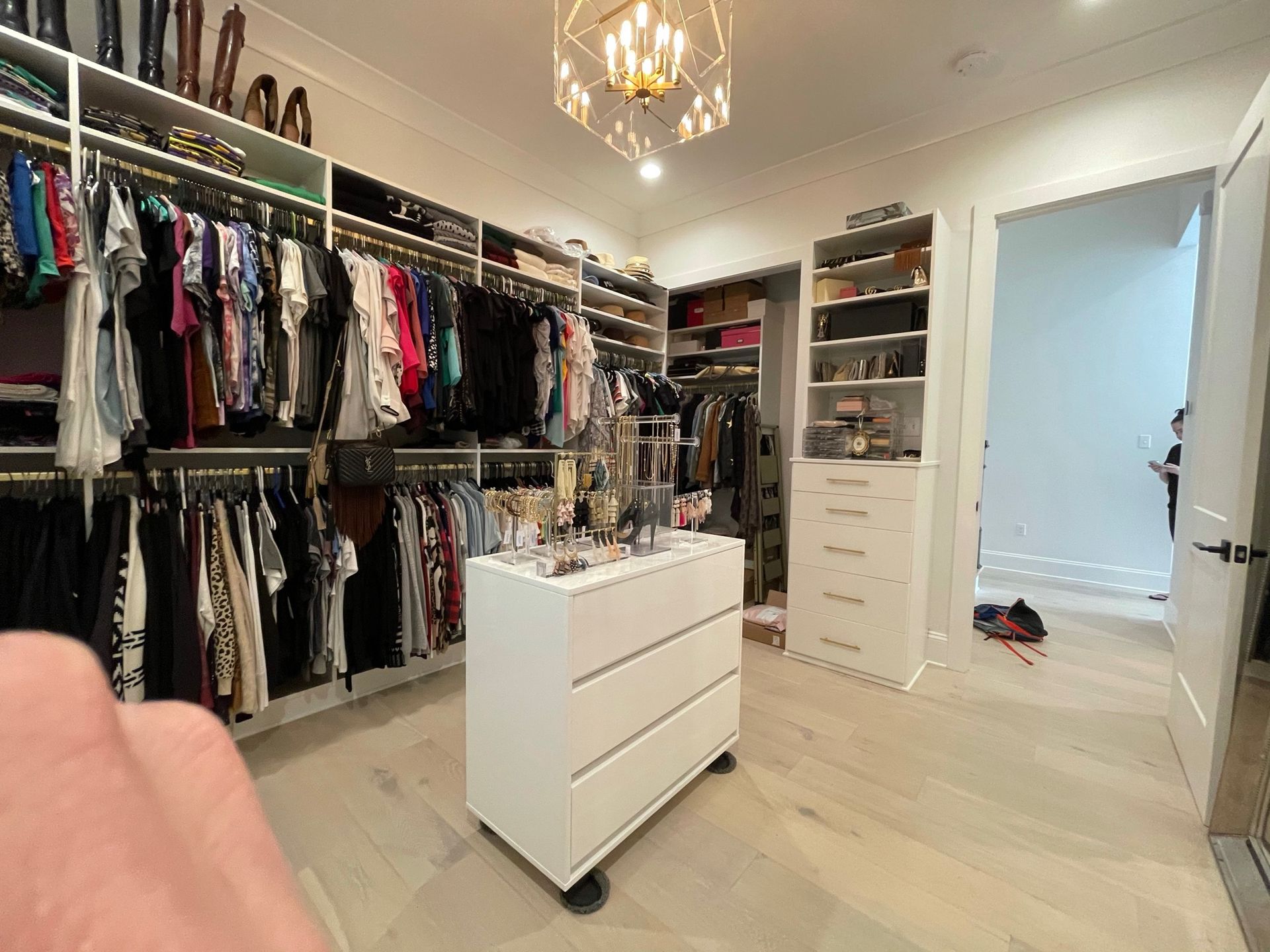 Walk-in closet with organized clothing racks, shelves, and a central dresser on wheels; light wood floor.